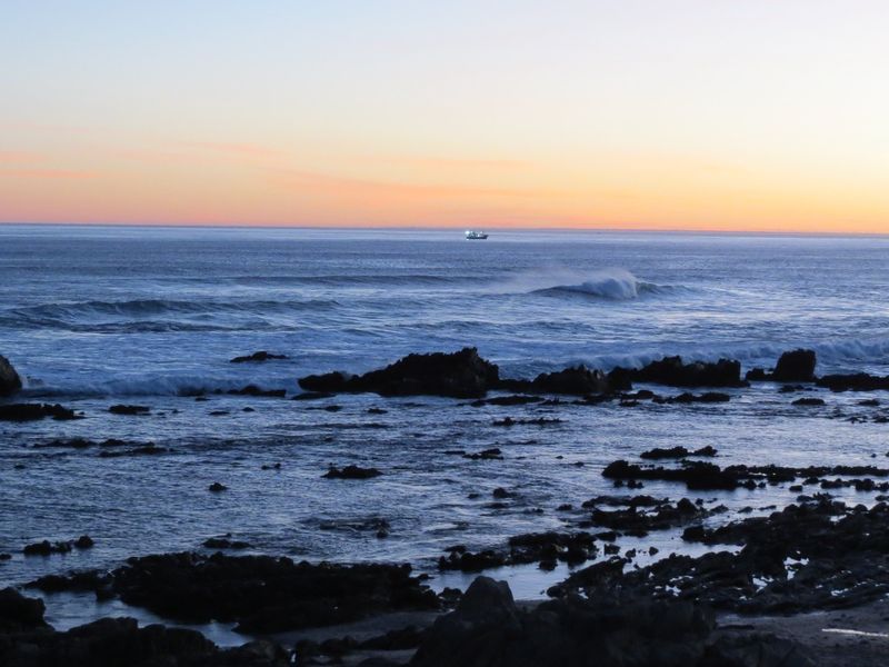 A scenic ocean view featuring rocky coastline and sunset horizon.