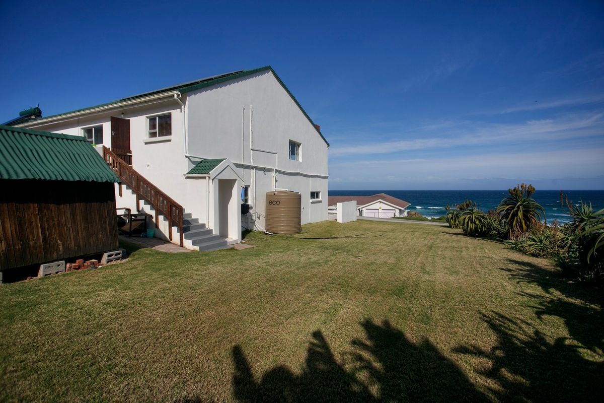 Rear view of the property featuring a spacious lawn, external staircase, and a water tank, with ocean views in the background.