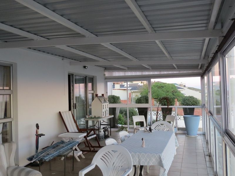 A covered, enclosed patio area featuring tiled flooring, a corrugated metal roof, and large glass windows offering an airy, versatile outdoor living space.