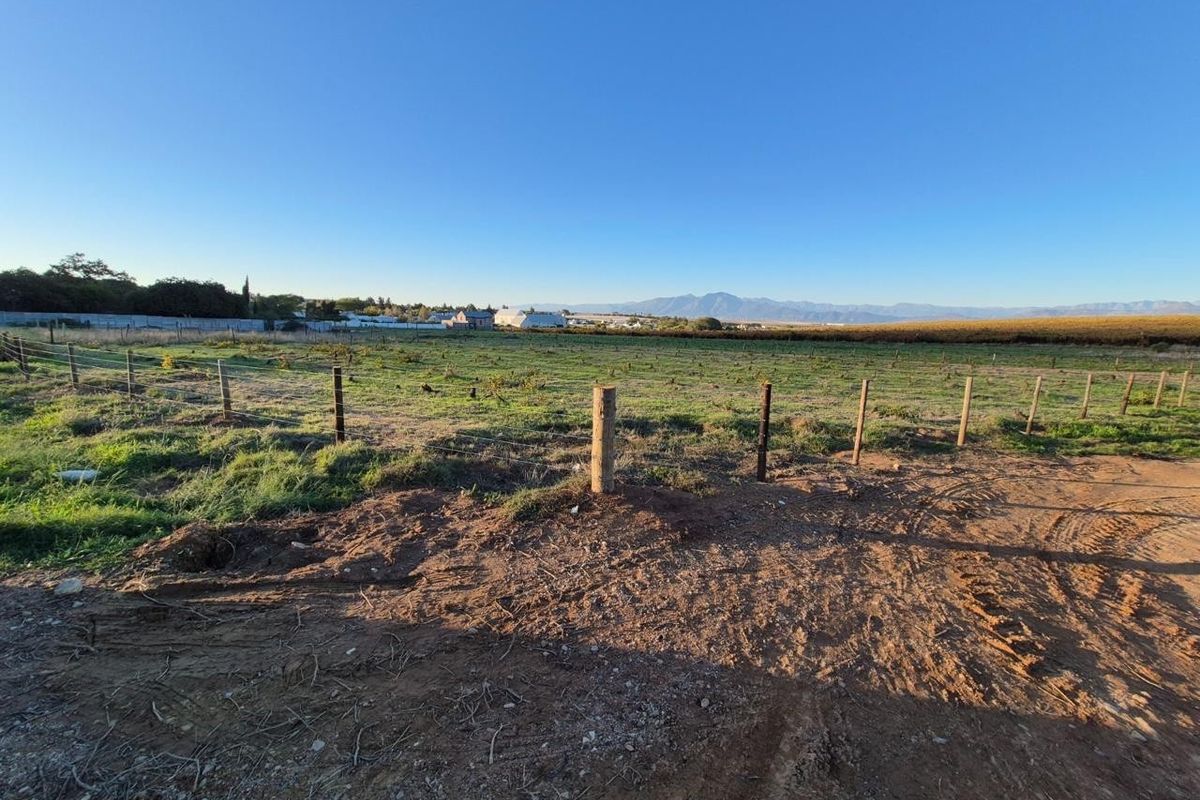 Expansive open land area featuring wire fencing and wooden posts, offering clear views of the surrounding landscape and distant mountains.