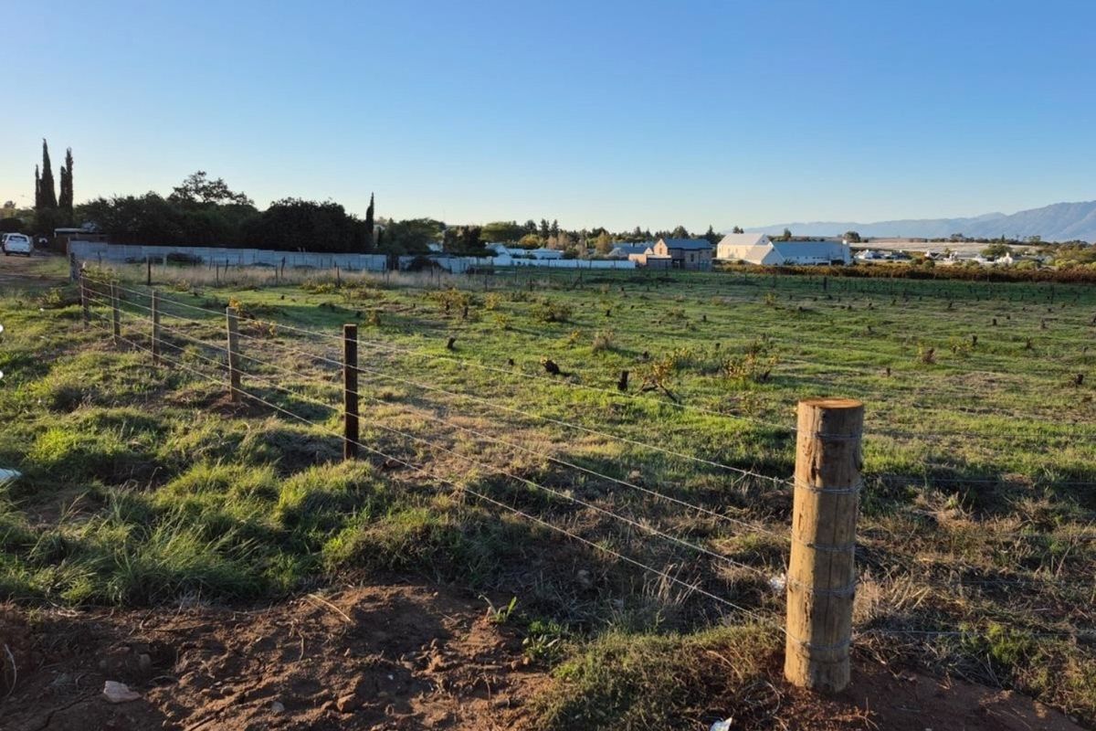 An expansive open plot of land featuring wire fencing and wooden posts, offering a clear view of the surrounding landscape and distant buildings.
