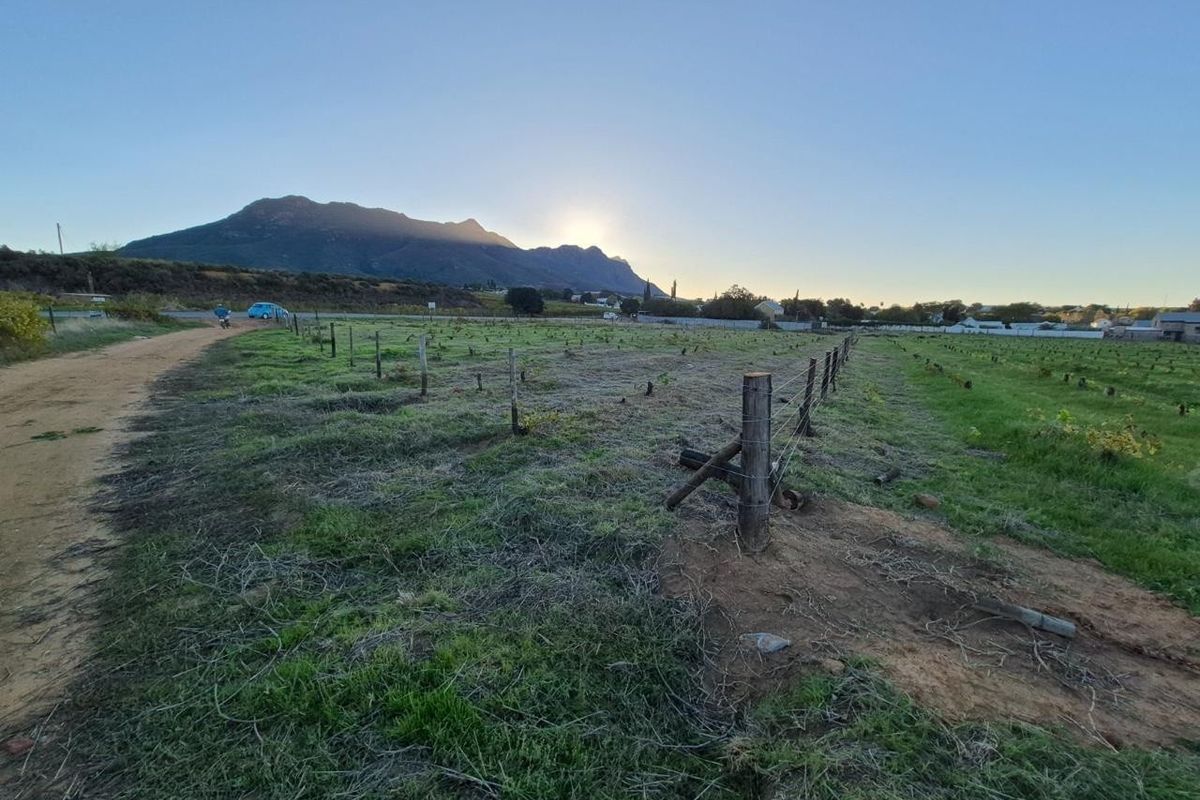 A scenic view of the small holding land featuring wire fencing, wooden posts, and a dirt track with mountain vistas in the background.