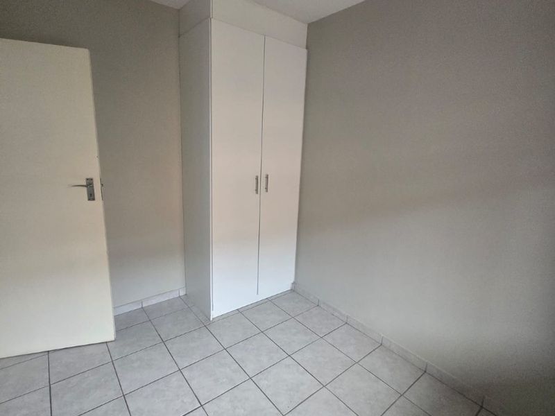 A clean, empty bedroom featuring neutral wall tones, tiled flooring, and a functional built-in wardrobe.