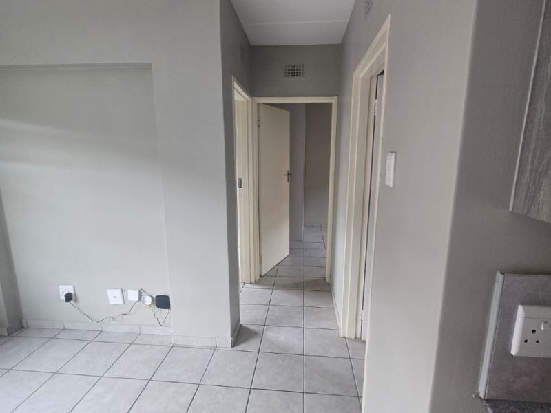A clean, neutral-toned hallway featuring tiled flooring and access to multiple rooms, providing a functional and well-maintained transition space within the apartment.