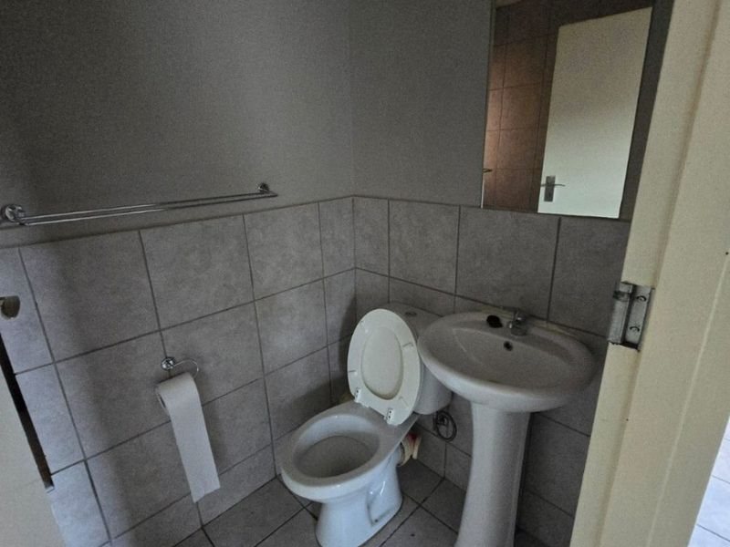 A compact guest bathroom featuring a pedestal basin, toilet, and neutral wall and floor tiling.