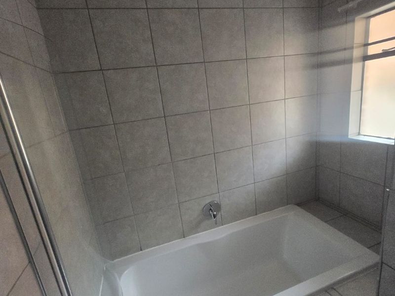 A functional bathroom featuring a built-in bathtub with shower head, neutral wall tiling, and a window for natural light and ventilation.
