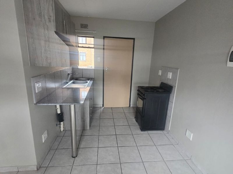 A compact kitchen featuring grey cabinetry, granite countertops, a stainless steel sink, and tiled flooring. The space is clean and ready for personalization.