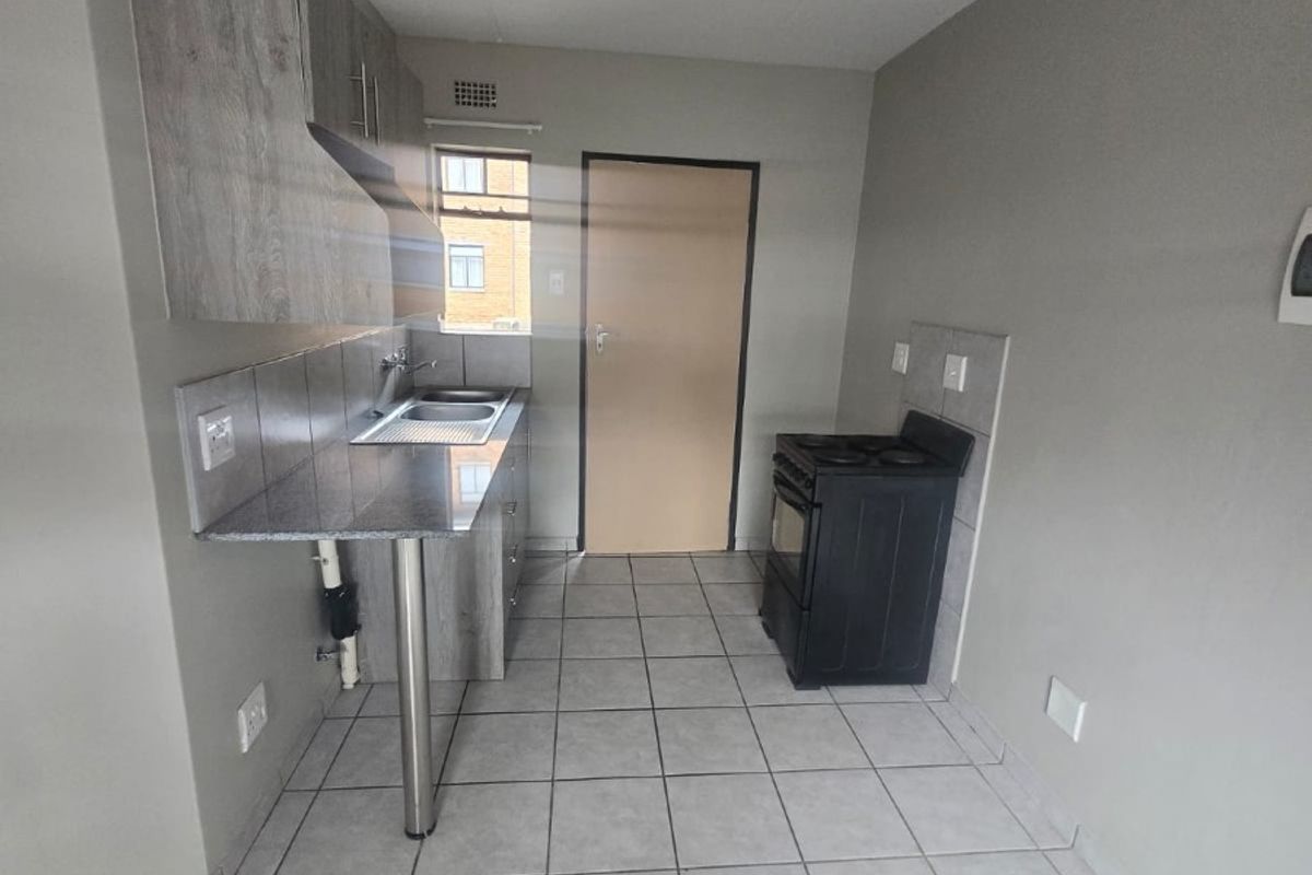 A compact kitchen featuring grey cabinetry, granite countertops, a stainless steel sink, and tiled flooring. The space is clean and ready for personalization.