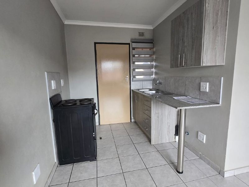A compact kitchen featuring built-in cabinetry, granite countertops, a stainless steel sink, and tiled flooring, presenting a clean and functional space.