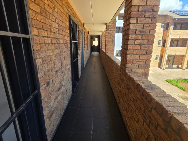 An exterior apartment walkway featuring exposed brick walls, tiled flooring, and secure metal gates leading to individual units.