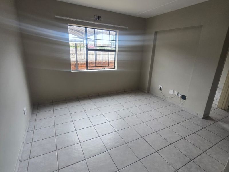 An empty living area featuring neutral tiled flooring, a window with security bars, and standard electrical points.