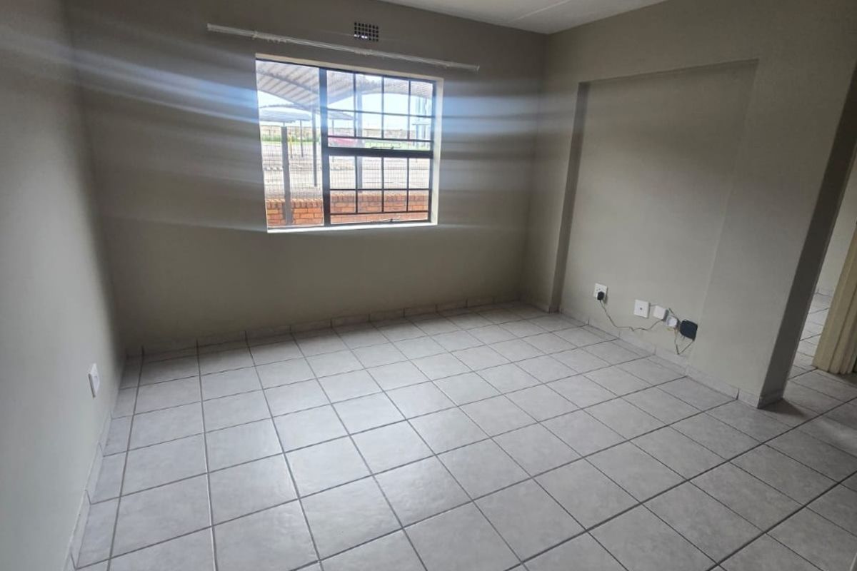 An empty living area featuring neutral tiled flooring, a window with security bars, and standard electrical points.