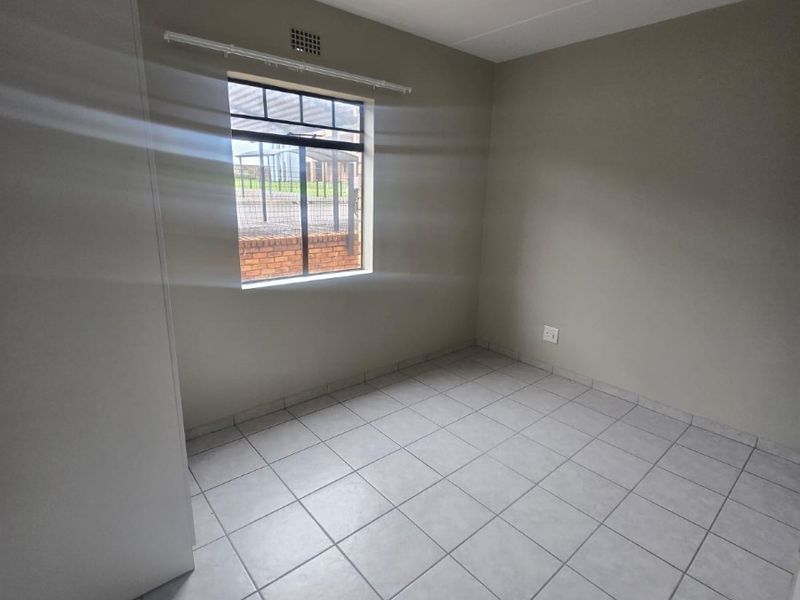 A clean, empty bedroom featuring neutral tiled flooring, a built-in cupboard, and natural light from a single window.