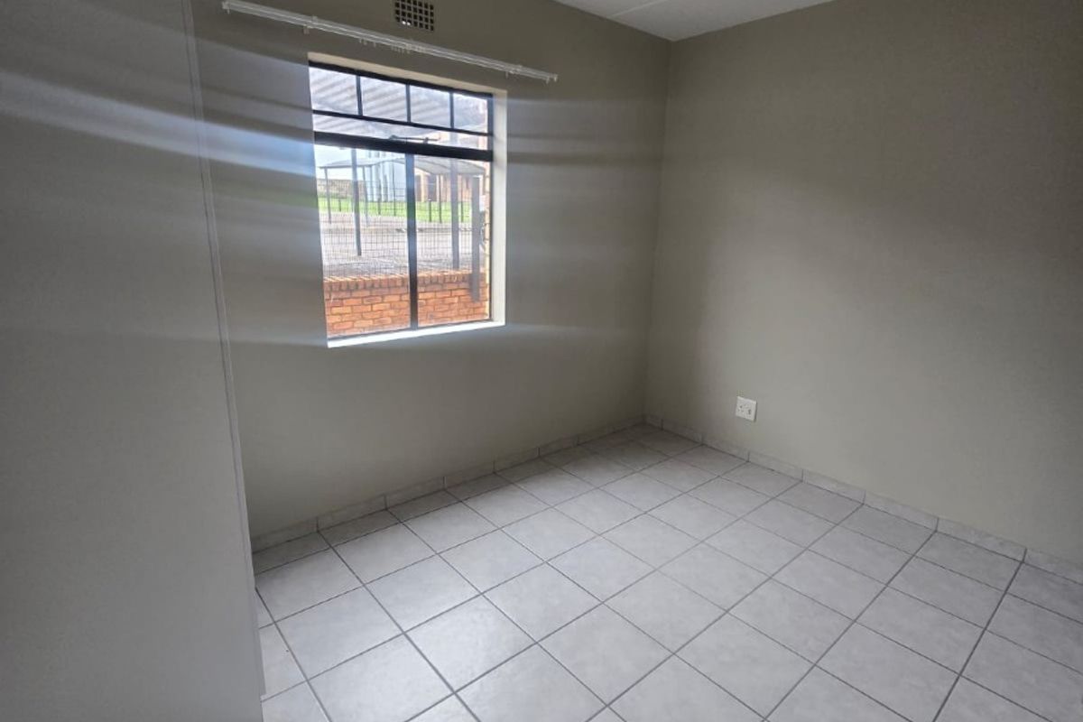 A clean, empty bedroom featuring neutral tiled flooring, a built-in cupboard, and natural light from a single window.