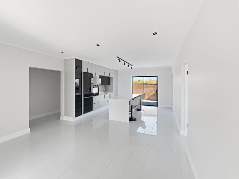 Modern kitchen featuring a central island, sleek cabinetry with integrated appliances, high-gloss tiled flooring, and recessed lighting, leading to an outdoor area.