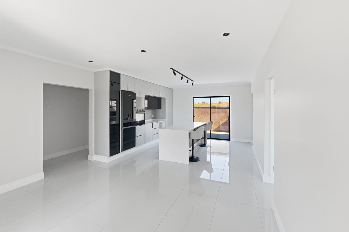 Modern kitchen featuring a central island, sleek cabinetry with integrated appliances, high-gloss tiled flooring, and recessed lighting, leading to an outdoor area.