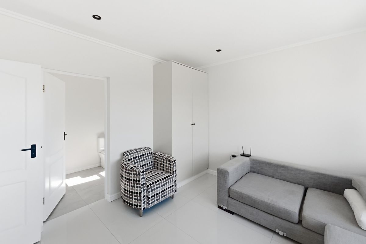 A bright bedroom featuring neutral tiled flooring, recessed downlighting, and a built-in wardrobe, with an adjoining en-suite bathroom visible through the doorway.