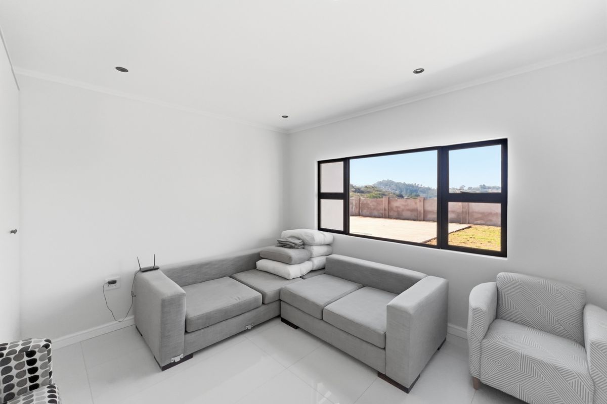 A bright living room featuring modern tiled flooring, recessed downlights, and large black-framed windows offering a view of the outdoor area.