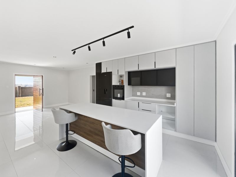 Modern kitchen featuring a central island, sleek built-in cabinetry, integrated oven, and high-gloss tiled flooring with direct access to the outdoor area.