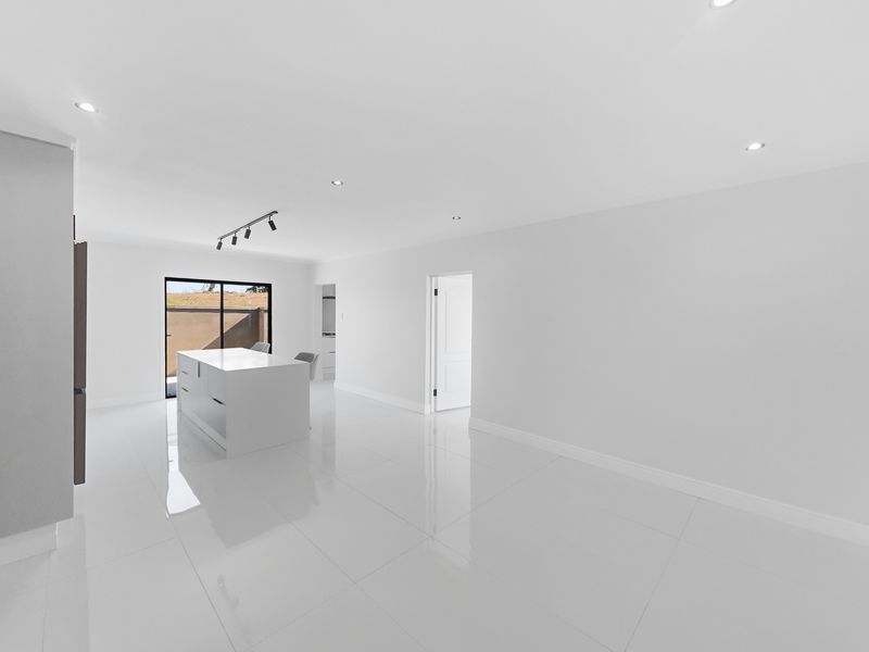 A bright, modern open-plan living and kitchen area featuring high-gloss tiled flooring, a central kitchen island, and recessed lighting throughout.
