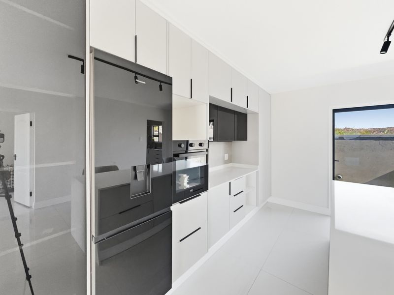 Modern kitchen featuring sleek white cabinetry, integrated appliances, stone countertops, and large format floor tiles with direct access to the outdoor area.