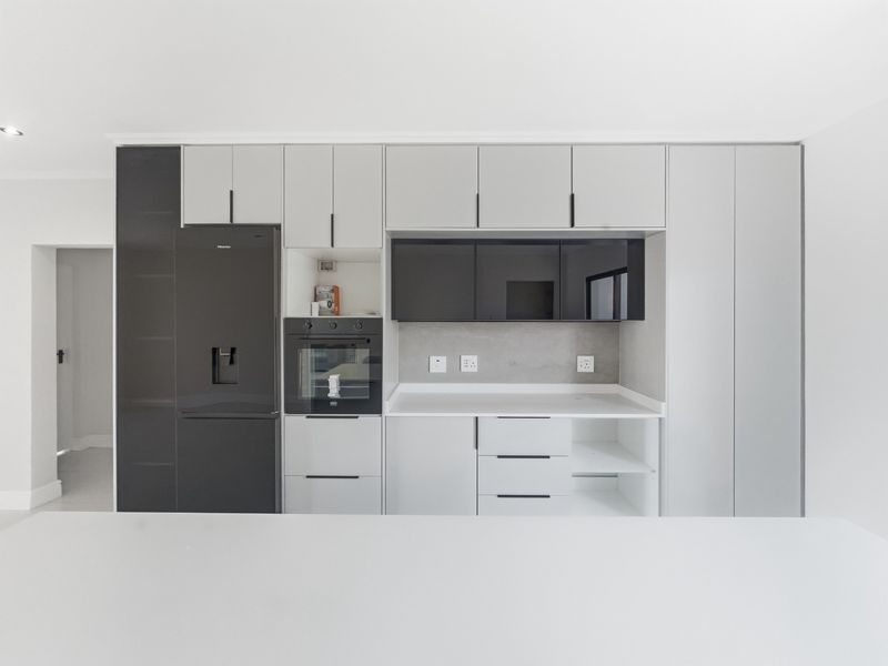 Modern kitchen featuring sleek grey and black cabinetry, integrated oven, and clean stone countertops in a minimalist, well-maintained space.