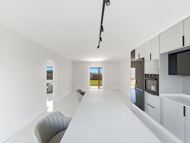 Modern kitchen featuring sleek built-in cabinetry, integrated appliances, stone countertops, and minimalist track lighting, leading to an outdoor area.