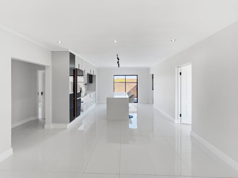 Modern, minimalist kitchen featuring a central island, sleek cabinetry, high-gloss tiled flooring, and recessed lighting, creating a bright and open culinary space.