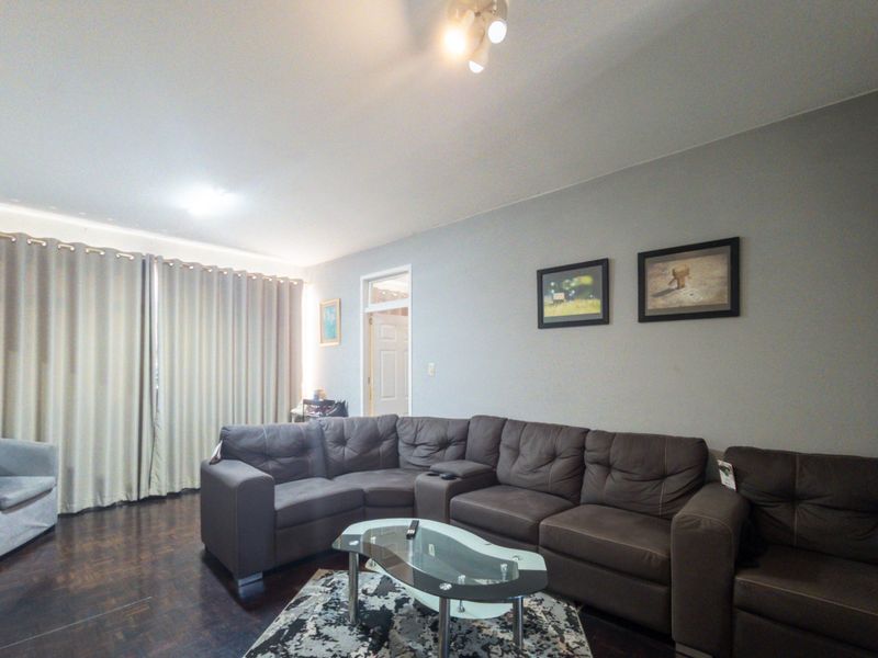 A spacious living room featuring dark parquet flooring, neutral wall tones, and large floor-to-ceiling curtains providing access to natural light.