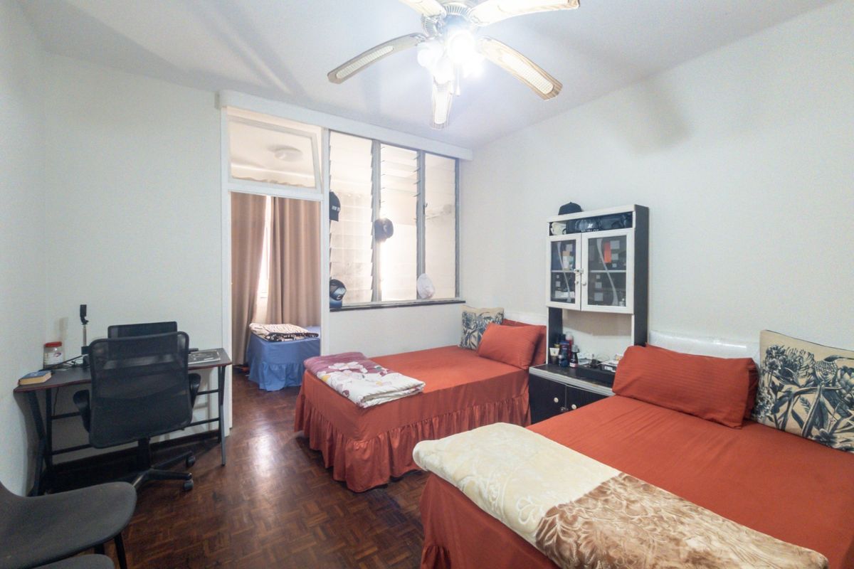 A bedroom featuring parquet flooring, a ceiling fan, and a built-in shelving unit, with an adjoining space visible through an internal window.