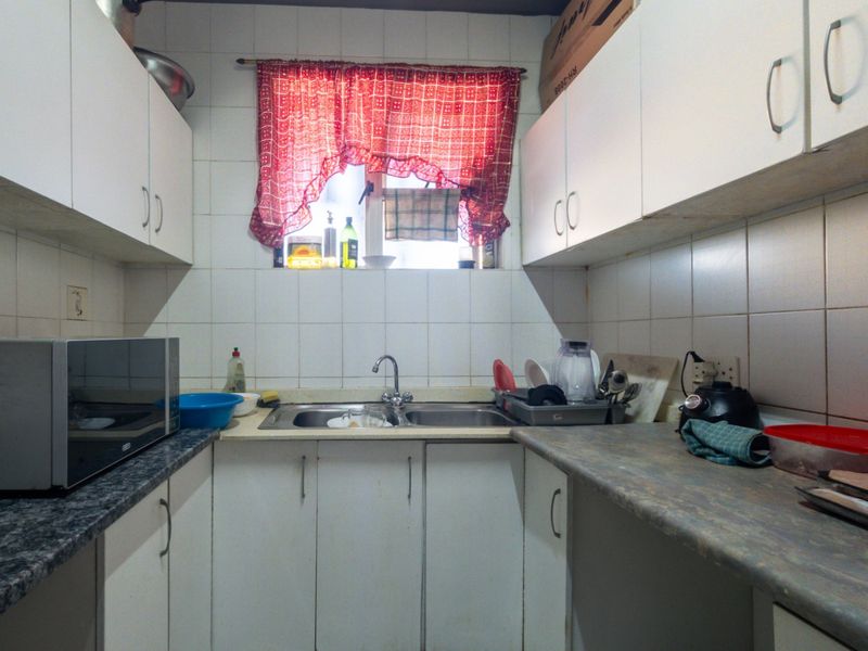 A compact kitchen featuring white cabinetry, laminate countertops, and a double basin stainless steel sink with tiled backsplash.