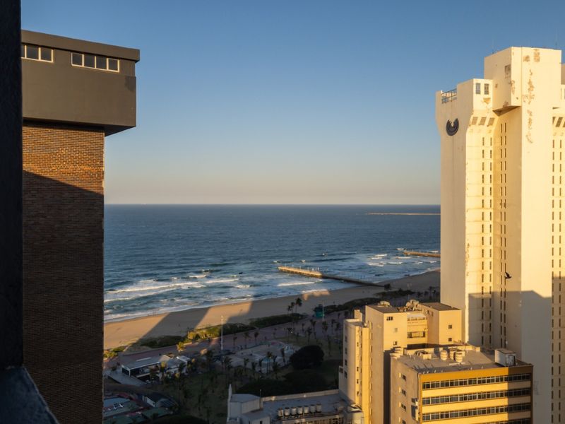 Elevated coastal view overlooking the beach, ocean, and surrounding urban apartment buildings.