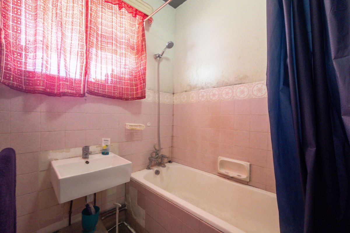 A dated bathroom featuring a bathtub, wall-mounted shower, and basin, requiring cosmetic updates and repairs to the wall finishes.