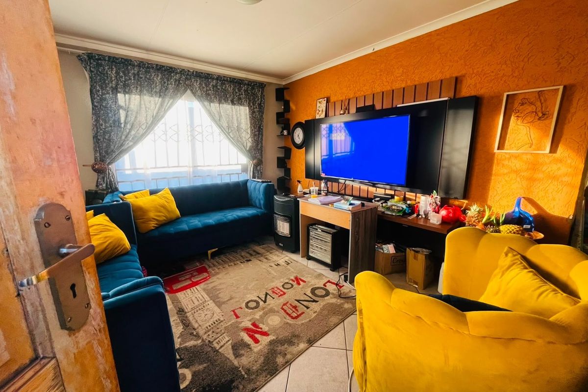 A compact living room featuring tiled flooring and a window with security bars, currently finished with textured orange wall paint.