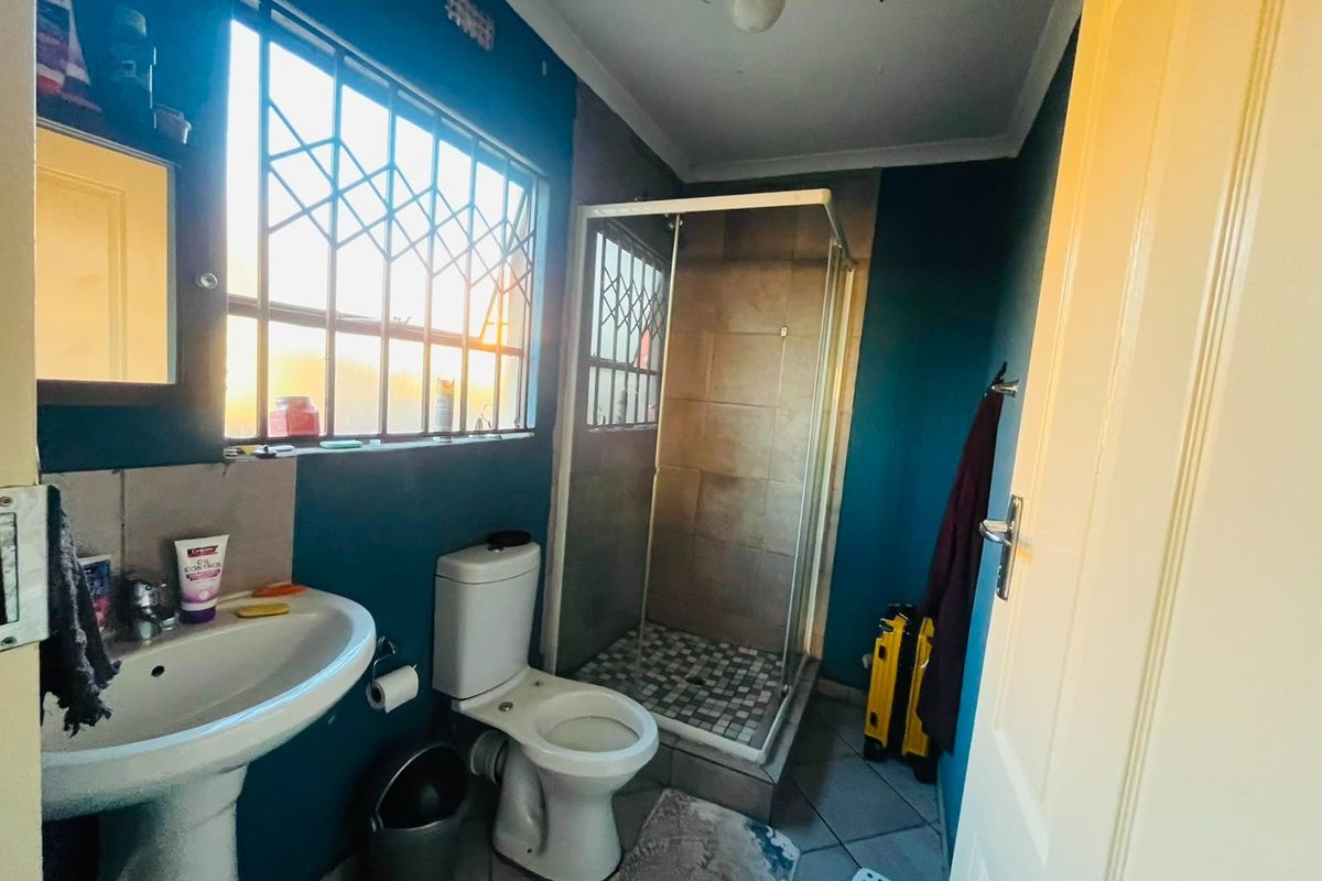 A functional bathroom featuring a pedestal basin, toilet, and a glass-enclosed shower with tiled flooring and security bars on the windows.