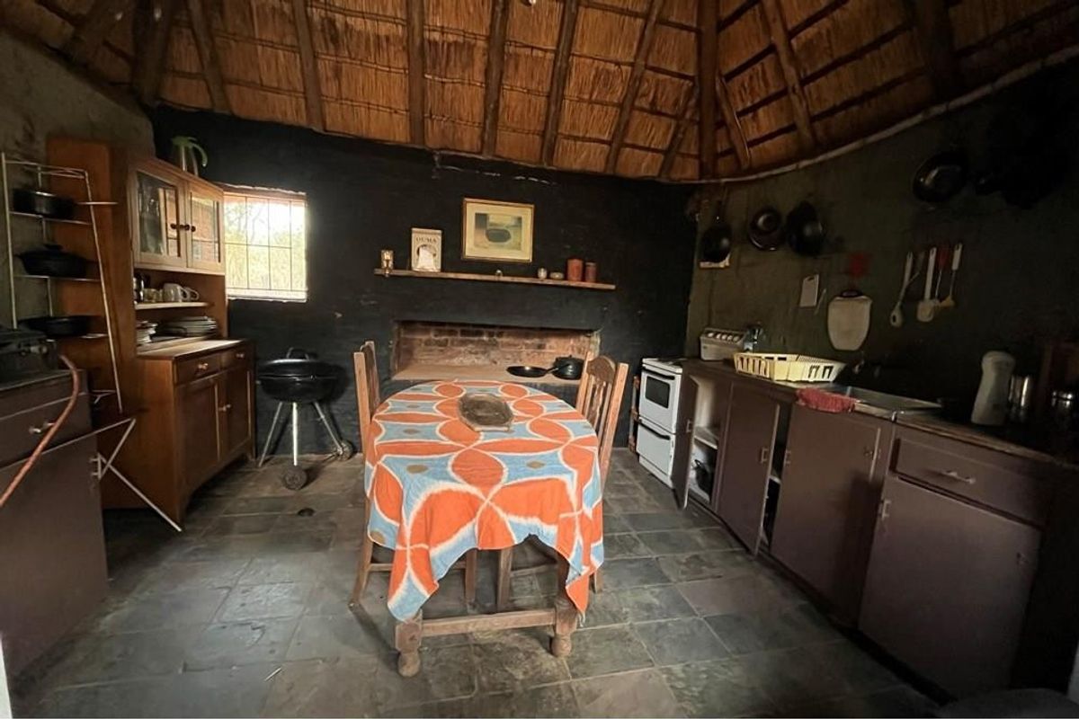 Rustic kitchen featuring a traditional thatched roof, stone flooring, and a built-in fireplace, offering a unique farm-style atmosphere.