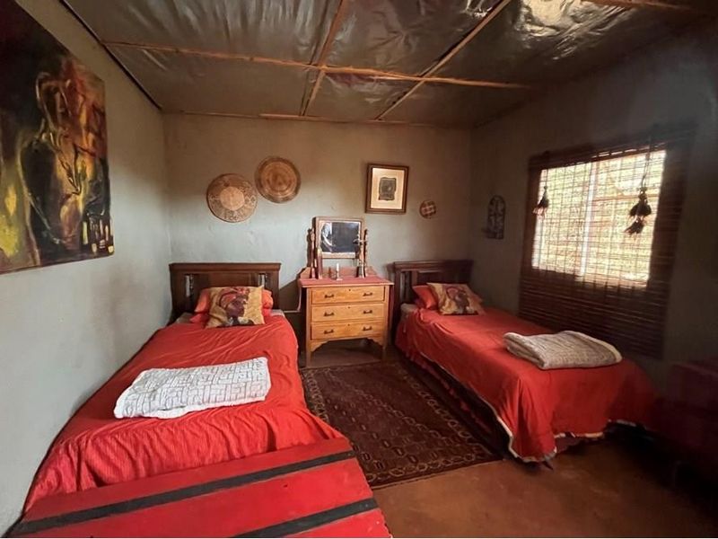 A rustic bedroom featuring exposed ceiling panels, textured walls, and a window with a bamboo blind, offering a simple and traditional farm-style aesthetic.