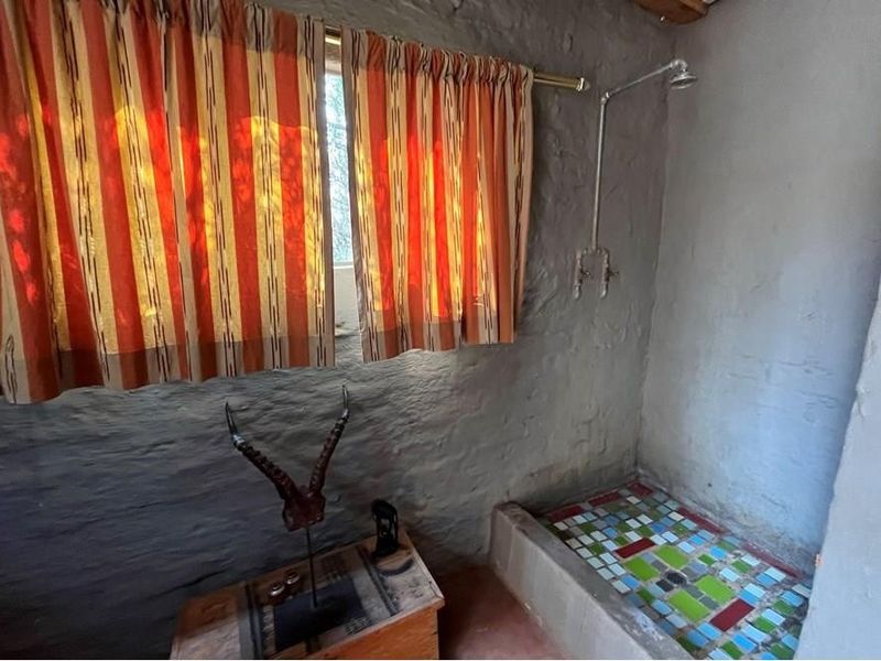 Rustic bathroom featuring textured stone walls, an exposed pipe shower, and a colorful mosaic-tiled shower floor.