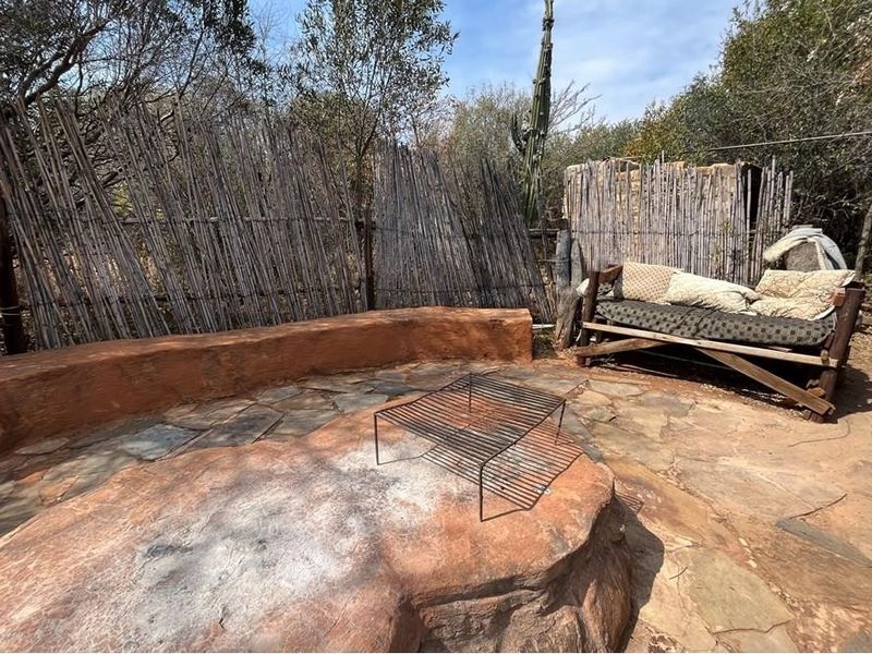 Outdoor patio area featuring a rustic stone-paved floor, a built-in stone fire pit, and a curved stone bench enclosed by natural reed fencing.