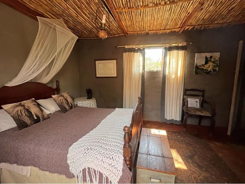 Rustic bedroom featuring a traditional thatched ceiling with exposed timber beams and warm tiled flooring, creating a cozy farm-style atmosphere.