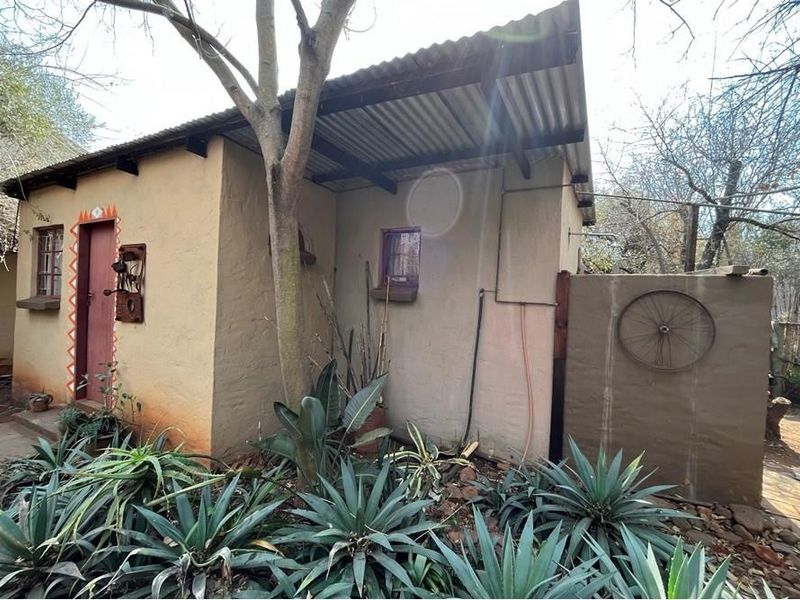 A rustic farm-style outbuilding featuring plastered walls, a corrugated iron roof, and an external shower installation set within a natural garden environment.