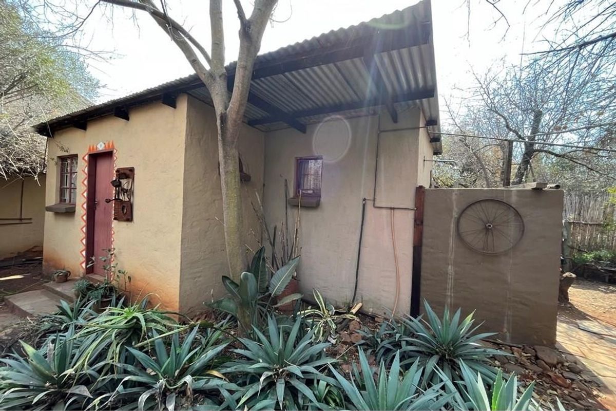 A rustic farm-style outbuilding featuring plastered walls, a corrugated iron roof, and an external shower installation set within a natural garden environment.