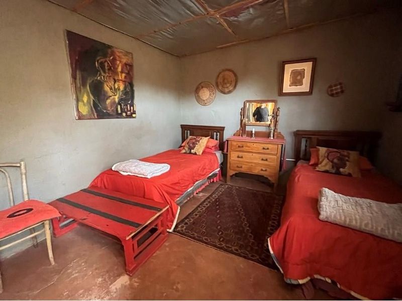A rustic bedroom featuring exposed ceiling beams and unfinished wall textures, offering a simple, traditional aesthetic suitable for renovation or restyling.
