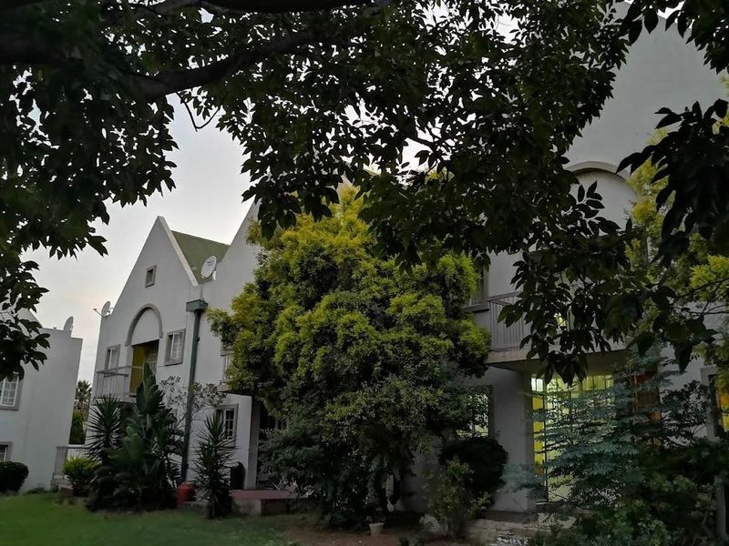 A view of the rear elevation of the apartment building featuring balconies, pitched roof architecture, and established garden surroundings.