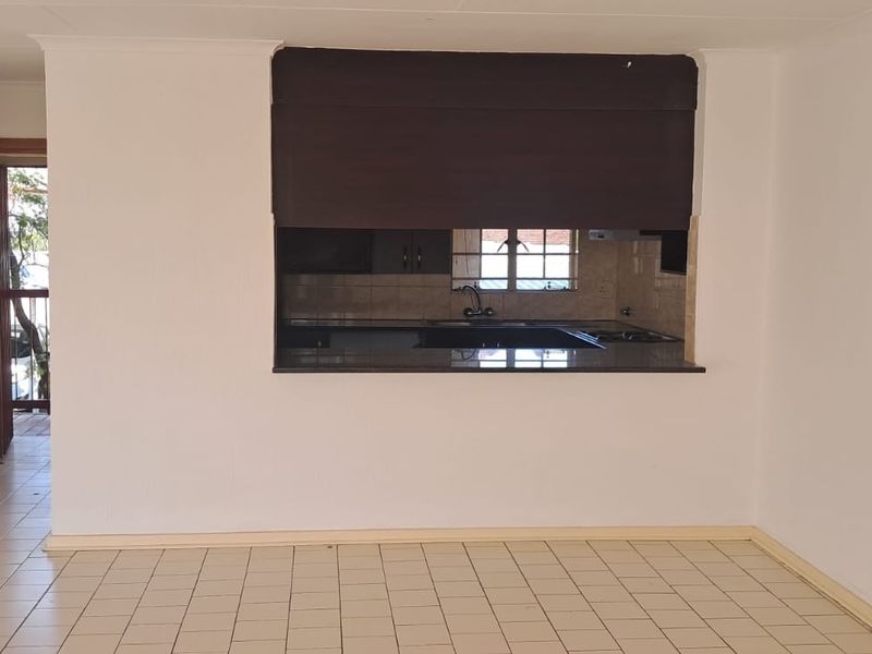 An open-plan living area featuring tiled flooring and a kitchen pass-through window with granite countertop, connecting to the kitchen space.