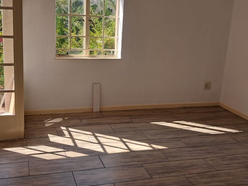 An empty bedroom featuring wood-look tiled flooring, a window with security bars, and a glass-paneled french door leading to an outdoor area.