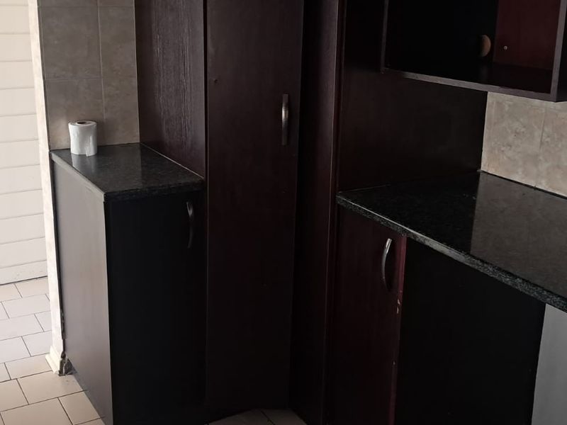 A compact kitchen area featuring dark wood cabinetry, granite countertops, and tiled flooring, providing a functional space ready for modernization.