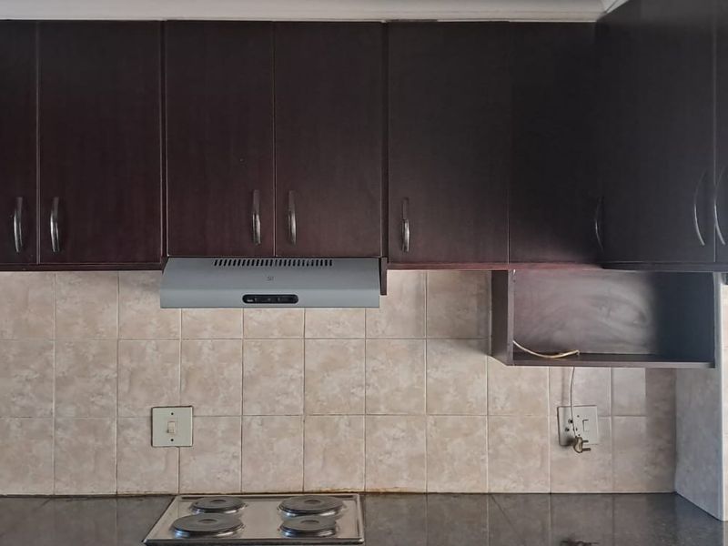 A functional kitchen area featuring dark wood cabinetry, a tiled backsplash, granite countertops, and a built-in electric hob with an extractor fan.