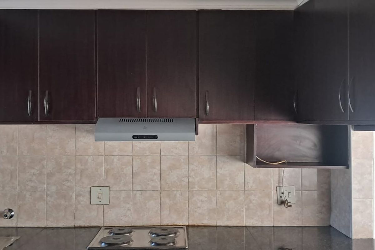 A functional kitchen area featuring dark wood cabinetry, a tiled backsplash, granite countertops, and a built-in electric hob with an extractor fan.