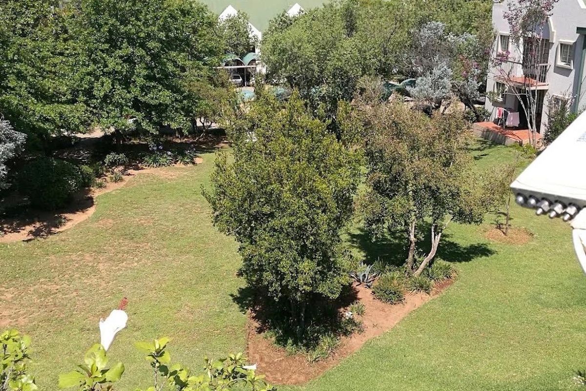 An elevated aerial view of a well-maintained communal garden area with mature trees and expansive lawn space within the apartment complex.
